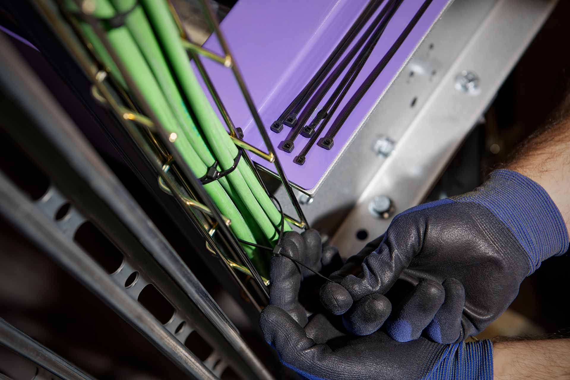 Mains d’un installateur protégées par des gants tenant des câbles avec colliers en Nylon® dans une installation électrique