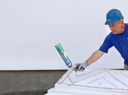 Technician applying ETICS polyurethane adhesive on insulation panels.