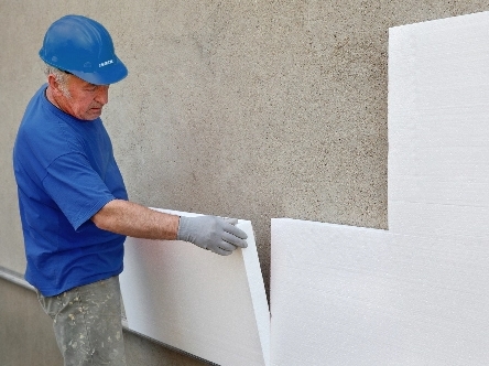 Technician installing ETICS insulation panels on wall after applying polyurethane adhesive